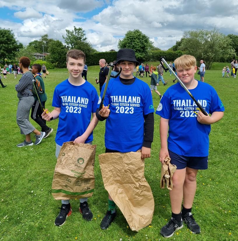 3 male students in uniform in a field holding litter grabbers