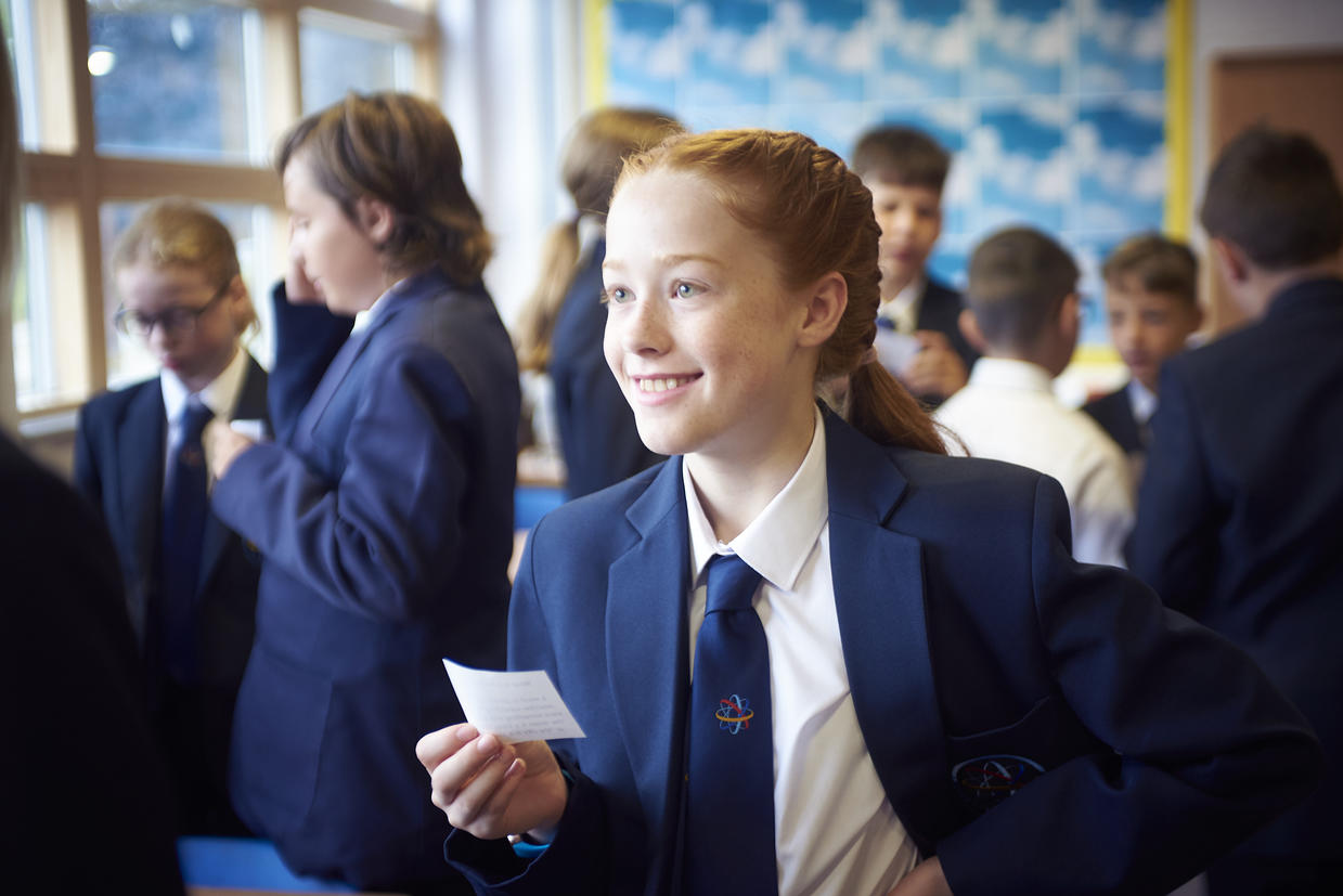 Female pupil with blond hair smiling holding a piece of paper