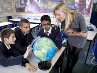 Teacher and three pupils look at globe