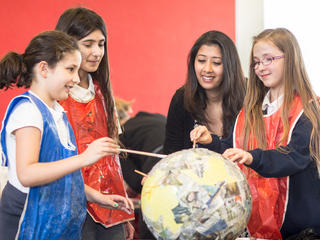 Children making papier mache globe as teacher looks on