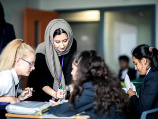 Female teacher looking at the work of two female secondary pupils
