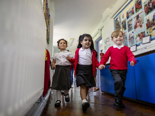 Primary pupils striding happily through a school corridor.