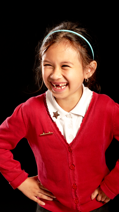 Young schoolgirl in red cardigan laughs in front of black background