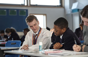 Teacher and pupil sat in classroom looking at work on a table