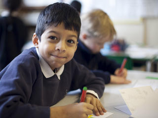 Young pupil seating at his desk writing