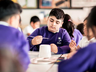 boy sitting in classroom, holding a paintbrush