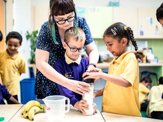 Image of primary teacher helping pupils to make a milkshake