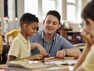 Image of primary teacher with pupil smiling and using counting beads