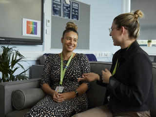 Image of two teachers smiling and chatting while sat on sofa