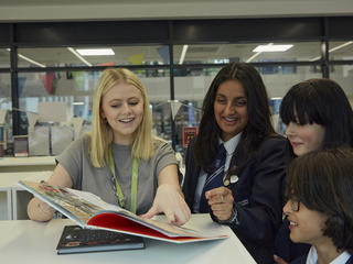 Image of teacher and pupils looking at book together and smiling in the library