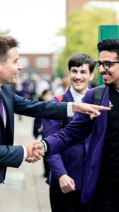 Male teacher enthusiastically shakes hand with Year 11 pupil as they leave the school gate.