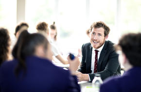 Image of teacher sat at table with pupils smiling