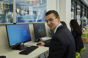 Smiling student in uniform using a computer in a classroom.